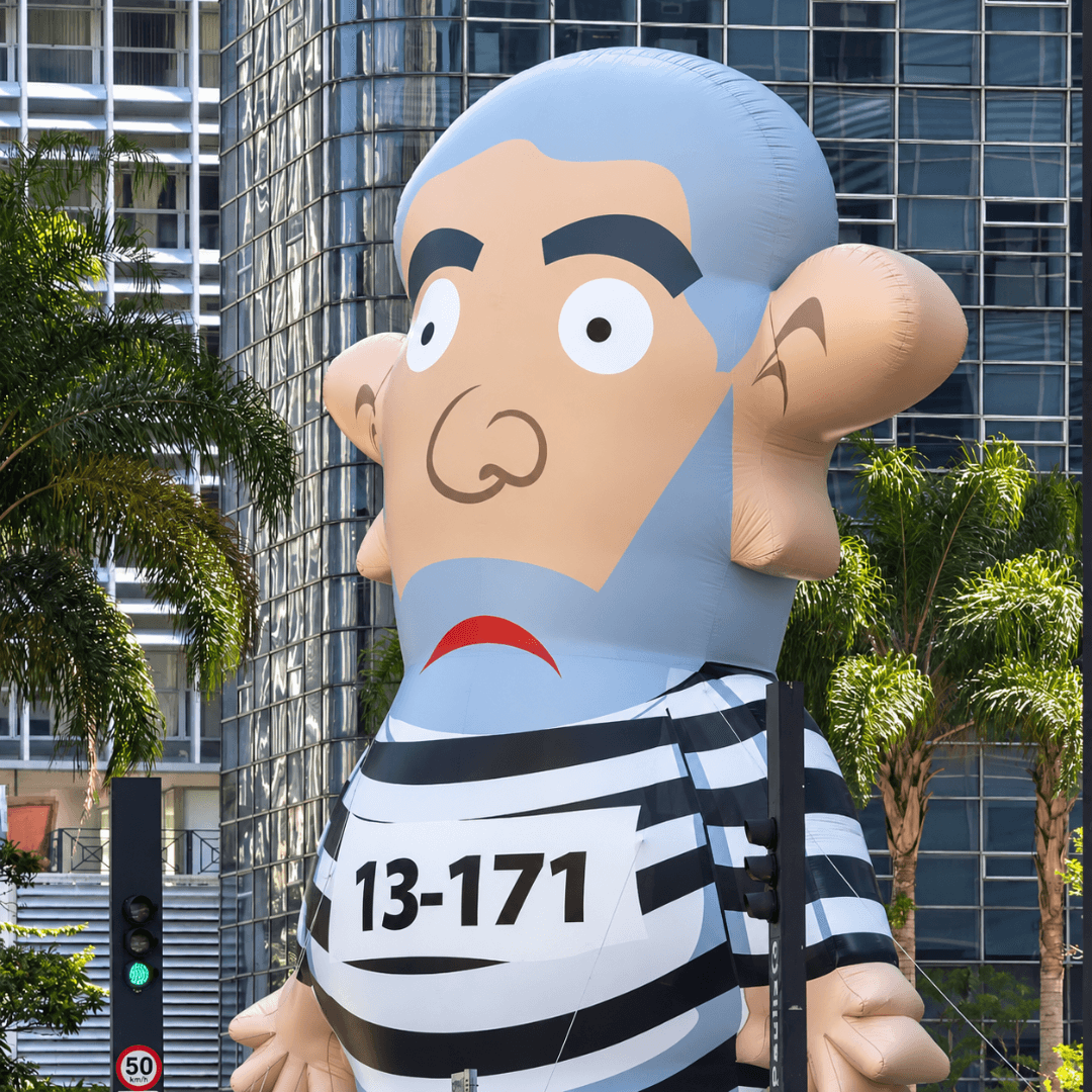 Inflável satírico com a identificação 13-171 exibido em via pública, entre prédios e palmeiras